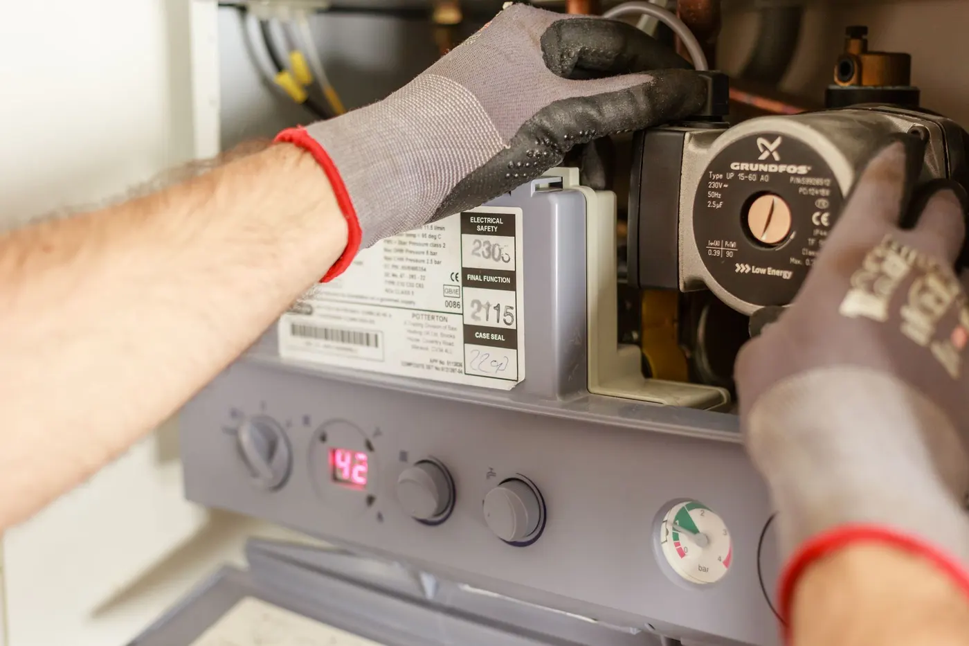 Engineer checking the pump and pressure gauge inside a wall-mounted boiler
